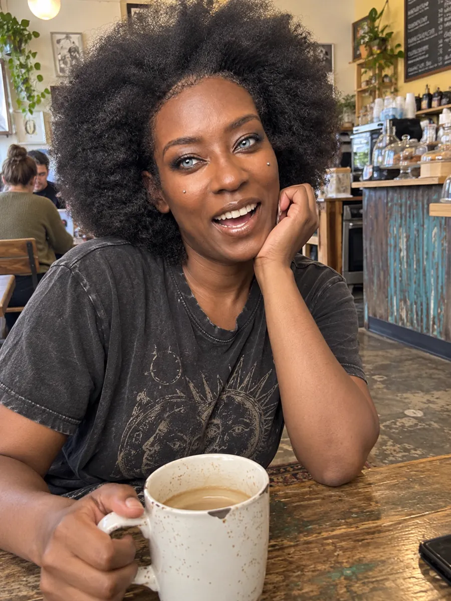 Silver smiling at a café table with a mug of coffee