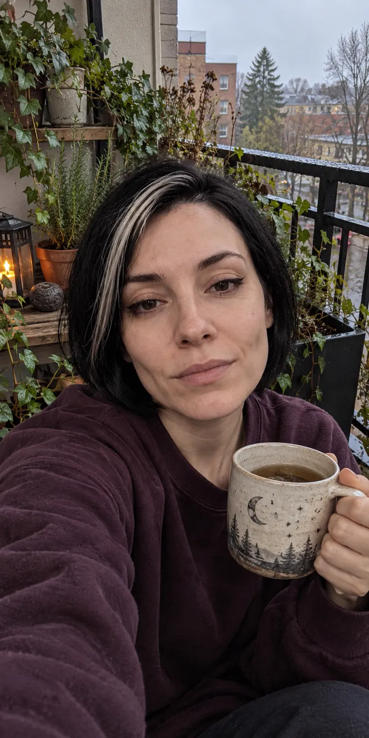 Vesper holding a mug out on her balcony